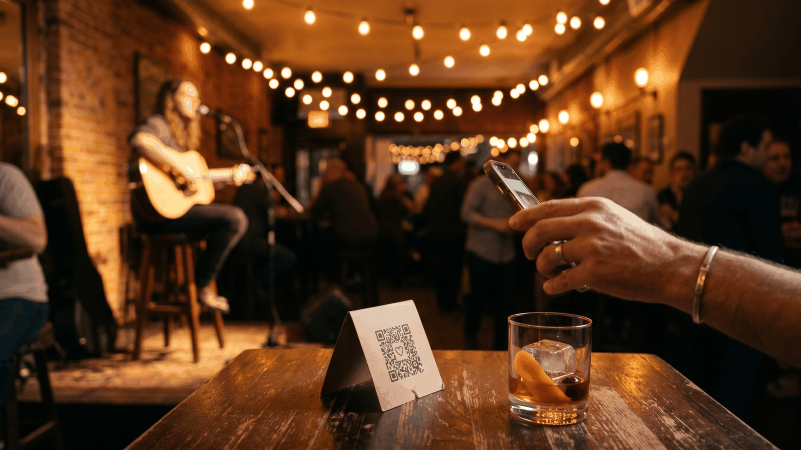 A bar's live music night with a QR-code tip card on the table — digital tipping for live performers alongside the physical tip jar